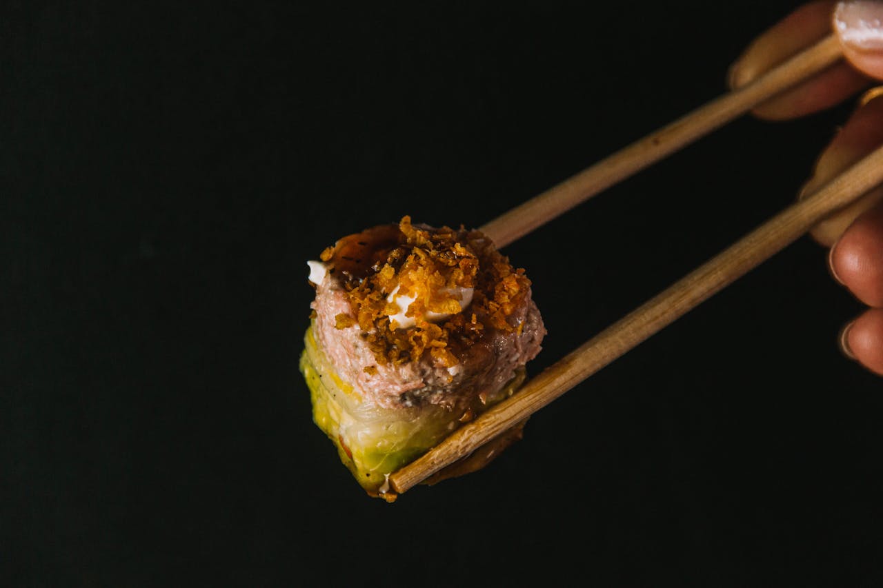 A vibrant sushi roll held with chopsticks against a dark background, showcasing appetizing textures.