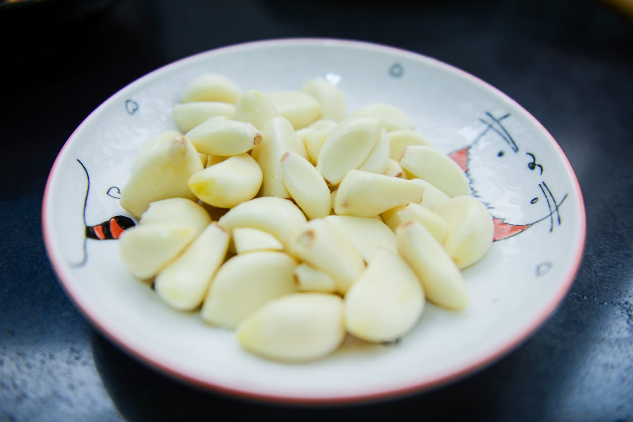 A close-up photo of peeled garlic cloves arranged on a decorative plate, highlighting their freshness.