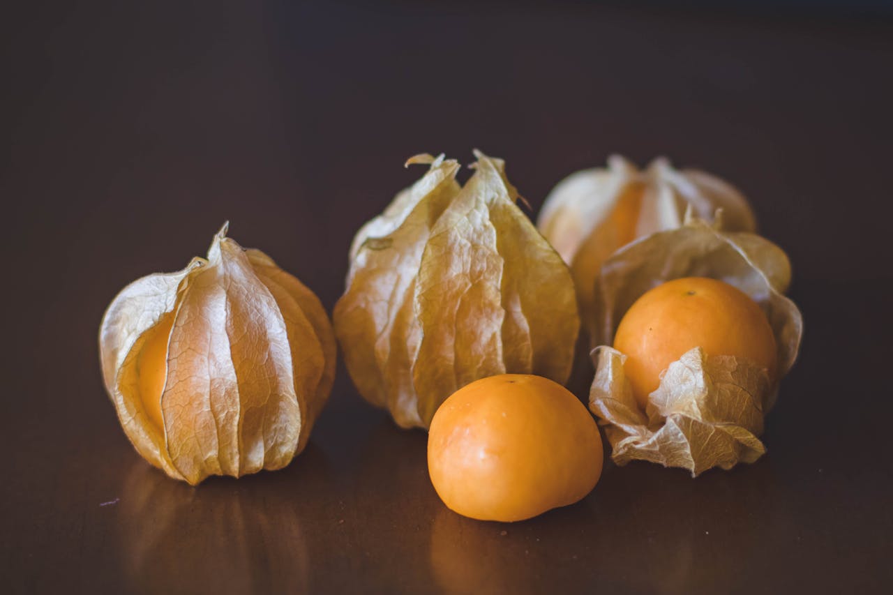 Close-up of fresh goldenberries with husks on a dark wooden table, showcasing their vibrant orange color.